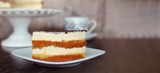 PIECE OF CAKE READY TO EAT SERVED WITH A CUP OF COFFE OR TEA AGAINST WOODEN TABLE.