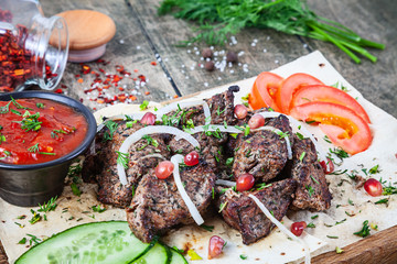 Close up grilled meat (pork) served on pita bread with onion, tomato and herbs, spices. Traditional eastern shashlik or kebab meat on wooden background. summer barbecue food with copy space