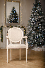 Classic Christmas decorated interior room New year tree. Christmas tree with gold decorations. Modern white classical style interior design apartment with fireplace and armchair.