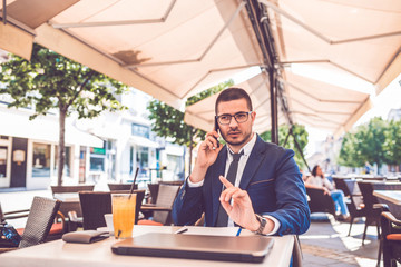 Young businessman in glasses talking on the phone during coffee break in a cafe