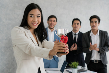 Worker holding trophy prize for best employees of the month in his hand. People in team celebrating as background.