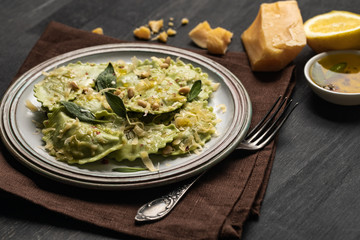 delicious green ravioli with sage, cheese and pine nuts served on black wooden table with fork, lemon and napkin