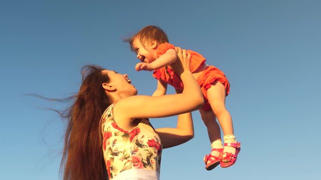 Mom plays with a small child against a blue sky. mother throws her daughter up to sky. happy family playing in the evening against sky. mother throws up the baby, baby smiles. slow motion filming.