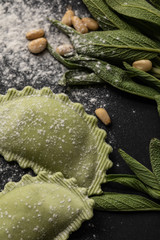 close up view of green ravioli, sage and pine nuts on black table