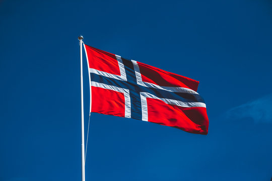 Norwegian flag against the blue sky. The wind blows against the blue sky without clouds