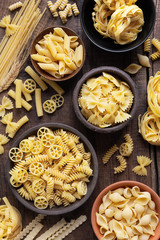 Variety of types and sshapes of dry Italian pasta in bowls against dark rustic wooden background