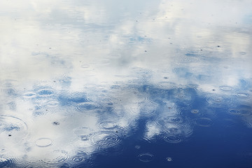 Reflection of clouds and circles from raindrops in the water of a lake. Abstract image, natural background.