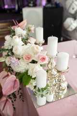 The wedding table setting for the newlyweds is decorated with fresh flowers of carnation, rose, anthurium and eucalyptus leaves. Silver candlesticks, white candles. Wedding floristry. Close-up details