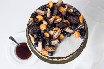 Cake with blueberries, blackberries, chocolate chip cookies and milk chocolate on a white plate with a cup of tea