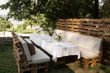 Wedding table setting decorated with fresh flowers in a brass vase. Wedding floristry. Banquet table for guests outdoors with a view of green nature. Bouquet with roses, eustoma and eucalyptus leaves