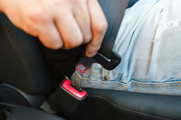 Close-up of car seat belt fastener. Men's hand fastens the seat belt of the car. Close your car seat belt while sitting inside the car before driving and take a safe journey.