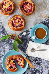 Table with yeasty sweet pastry with fresh cherries and streusel topping, cup of tea and few cubes of sugar. Summer fresh fruit appetizer.