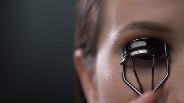 Woman corrects eyelashes with curling tongs, close up