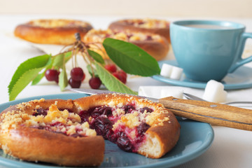 Table with yeasty sweet pastry with fresh cherries and streusel topping, cup of tea and few cubes of sugar. Summer fresh fruit appetizer.