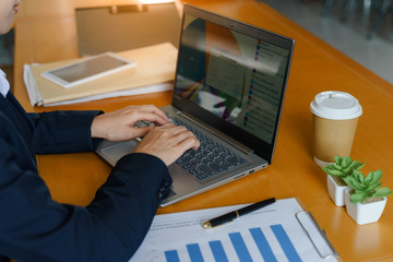 Close up of business person's hands uses laptop keyboard works in the office with cup of coffee on the wooden table. Business and office worker concept.