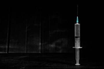 Empty syringe on dirty dark background with sharp light and shadows