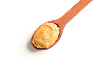 Creamy peanut butter in wooden spoon isolated on white background, top view. A traditional product of American cuisine
