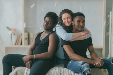 Multicultural love and relationships concept. Young white woman sits and hugs with two african dark...