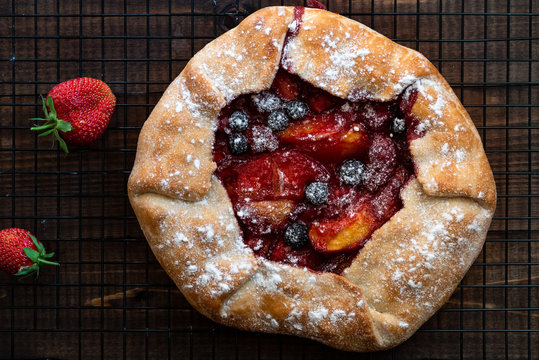 Mixed berry galette pie. Rustic berry galette tart with strawberries and blueberries with an open sweet filling on a dark wooden background. Top view, flat lay.
