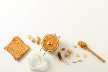 Flat lay composition with peanut butter sandwich, glass jar, peanut and spoon on white background,...