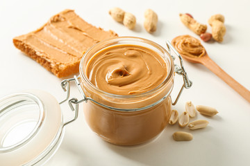 Composition with peanut butter sandwich, glass jar, peanut and spoon on white background, space for text and closeup