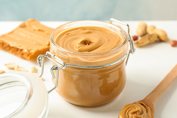 Composition with peanut butter sandwich, glass jar, peanut and spoon on white table against light background, space for text and closeup