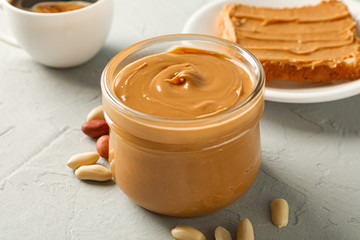 Glass jar with peanut butter, peanut, cup of coffee and peanut butter sandwich on grey background, closeup and space for text