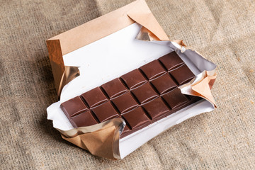 Chocolate bar in paper wrapper is lying on burlap.