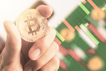 Close up hand holding bitcoin with background Candlestick chart make from color paper white and red on Green board with grid lines