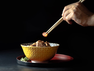 Hand use bamboo stick for Rice topped with pork isolated on black background, raw food Japanese food court concept.