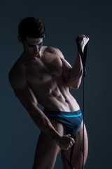 Fototapeta na wymiar Muscular fitness young male antique perfect muscles six packs of abs and bare chest. Bodybuilder model trains with a stretching elastic against a dark background in the studio. Workout training gym