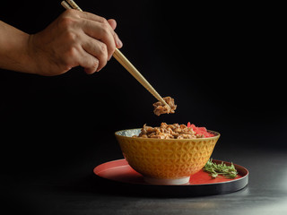 Hand use bamboo stick for Rice topped with pork isolated on black background, raw food Japanese food court concept.