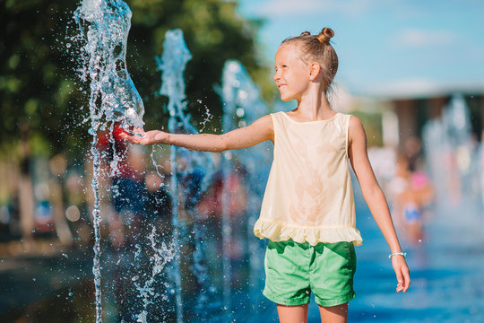 Little adorable girl have fun in street fountain at hot sunny day