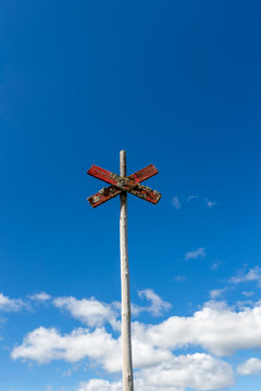 Old weathered wooden trail sign post with red cross against blue sky with clouds.