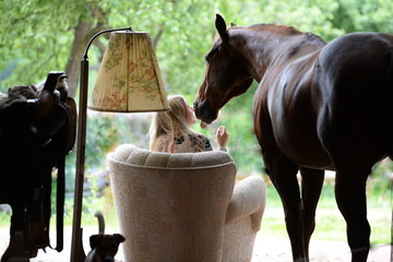 Freunde fürs Leben. Junge langhaarige Frau sitzt in einem Sessel neben ihrem Pferd © Grubärin