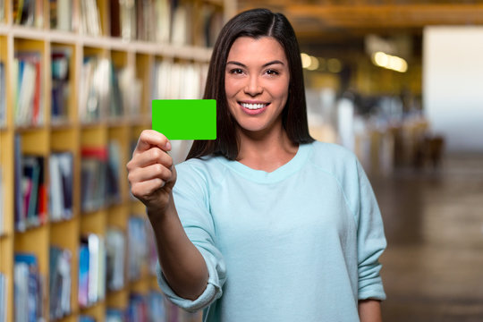 Smiling college university student holding blank card in library, possibly member, membership, i.d., identification, credit, debit, banking card