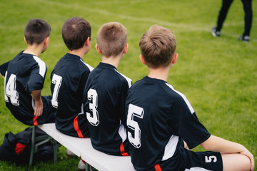Boys on Football Bench During Soccer Match. Coach of Youth Sports Team in the Background