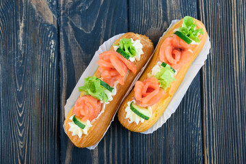 Tasty and beautiful eclairs on a wooden board. Appetizing dessert with red fish, cucumber, cheese and greens.