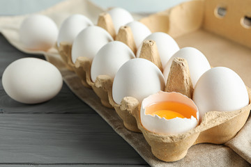 White chicken eggs in carton box on wooden table, space for text and closeup