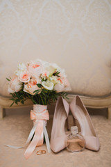 Botanic bridal chic. Bouquet with silk ribbons, female classic shoes, perfume bottle, wedding rings on vintage chair.