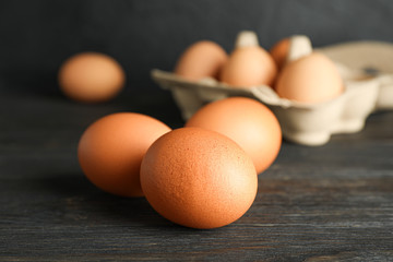 Brown chicken eggs in carton box on wooden table against black background, space for text and closeup