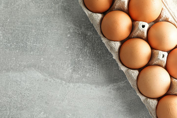 Brown chicken eggs in carton box on grey background, space for text and top view