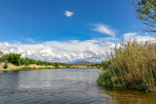 Beautiful Arizona landscape with a river, desert scenery and mountains in the distance. Puffy white clouds over purple mountains