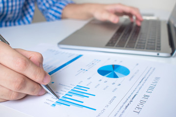 Close-up image of the hand of a business worker pointing graph with a pen on a modern white desk.