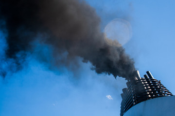 Ship funnel emitting black smoke in a blue sky, air pollution, carbon emissions, carbon tax, global...