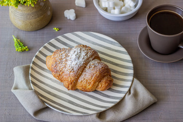 A croissant and coffee on a grey background. The flowers. Breakfast.