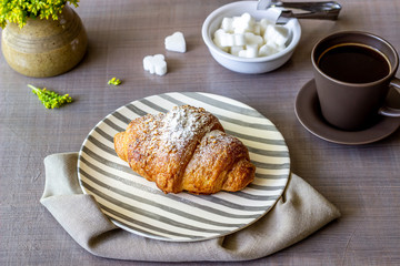 A croissant and coffee on a grey background. The flowers. Breakfast.