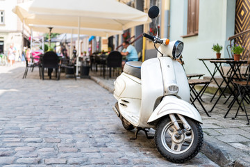 Closeup of white scooter parked by European cafe with bokeh background of outdoor restaurant in summer in Lviv or Lvov, Ukraine city © Andriy Blokhin