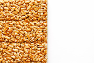 A large golden tile of sunflower seeds, a bar in a sweet molasses on a white background. Kozinaki useful and tasty sweets of the East