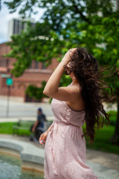 beautiful young Hispanic is having fun and smiling in a outdoor park in Chicago wearing a sexy pink summer dress. Latin model enjoys her stay downtown near this pretty landmark